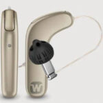 A beige behind-the-ear hearing aid with a black earpiece and a thin, transparent tube, shown from both side and front angles on a light background.
